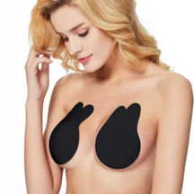Mulher loira de pele clara com expressão suave, usando adesivos pretos para sustentação dos seios. A imagem mostra o produto aplicado sobre a pele, com fundo branco.